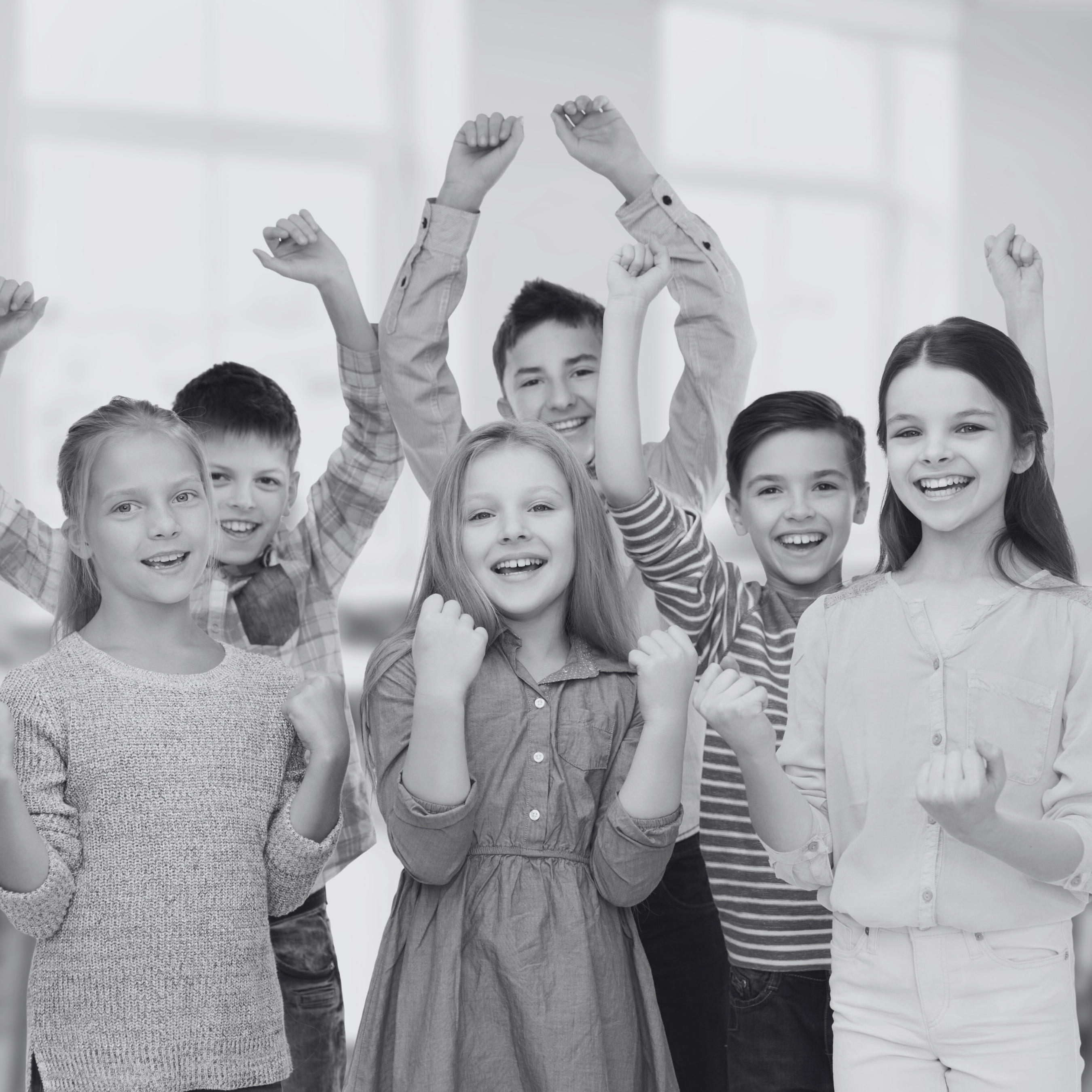Black and white photo of a diverse group of children smiling and raising their hands in celebration.