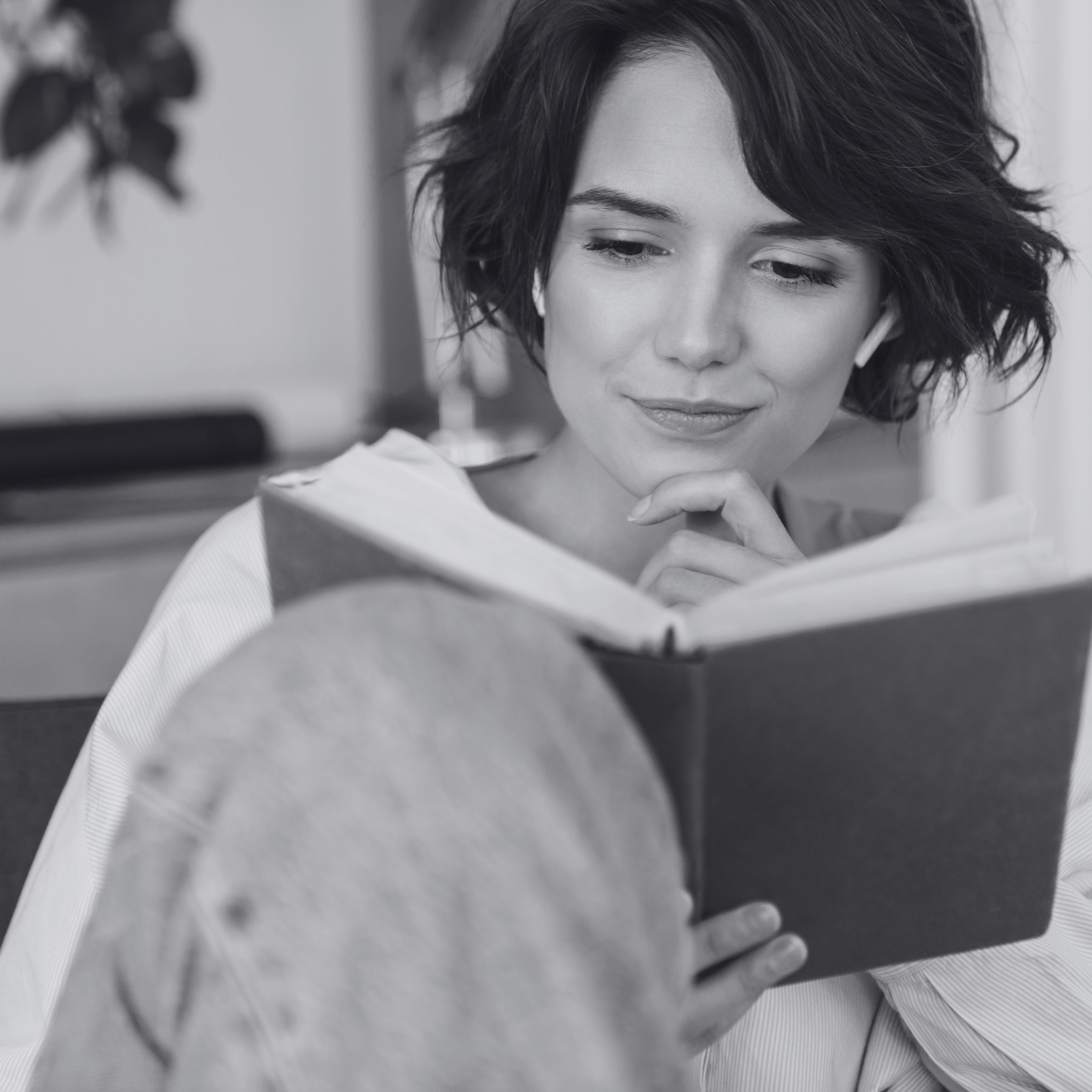 Black and white photo of a woman reading a book with a focused expression.